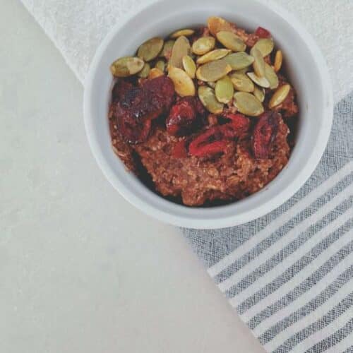 Chocolate Porridge on a tea towel topped with pumpkin seeds and dried cranberries