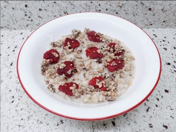 Bowl filled with cooked barley, roasted raspberries and topped with sesame seeds.