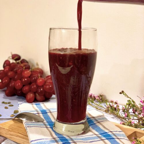 Red beet smoothie to lower blood pressure with grapes in the background on a checkered cloth