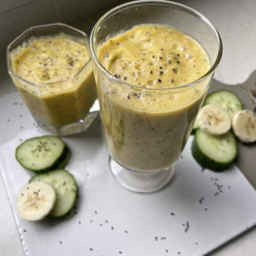 Two yellow pineapple smoothies for weight loss on a cutting board surrounded by cucumber, banana and chia seeds