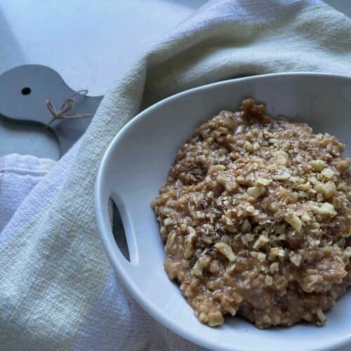 Vegan protein oatmeal in a white bowl surrounded by a beige cloth on grey cutting board on a white counter