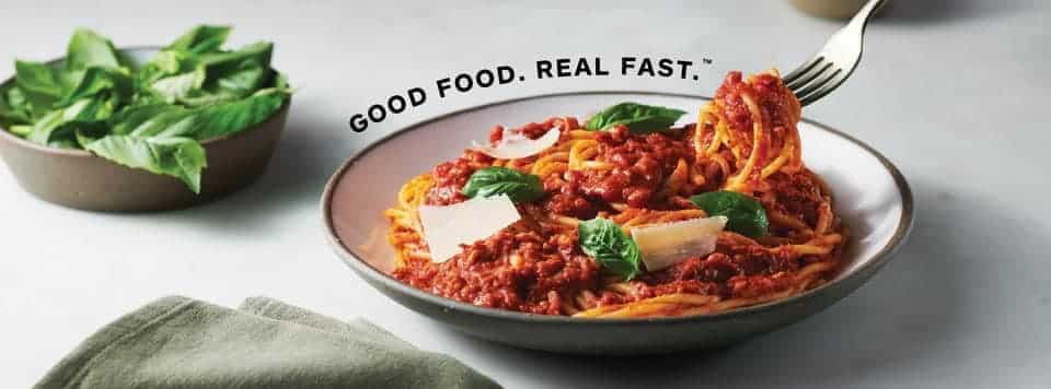 Bowl of spaghetti in a grey bowl with a side salad and grey napkin with Epicures slogan "food food real fast"