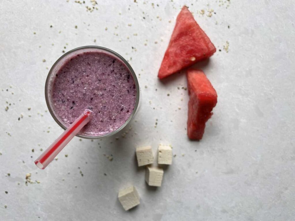 Top of watermelon smoothie with red striped straw and watermelon triangles and cubed tofu sitting beside the smoothie.