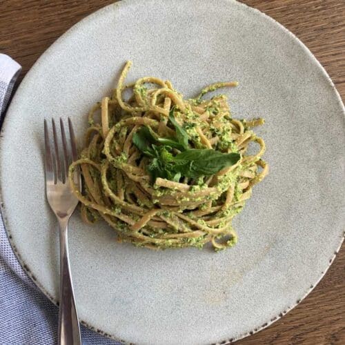 Edamame pasta sauce on whole wheat spaghetti noodles presented on a white plate, topped with basil and a fork on a wood table.