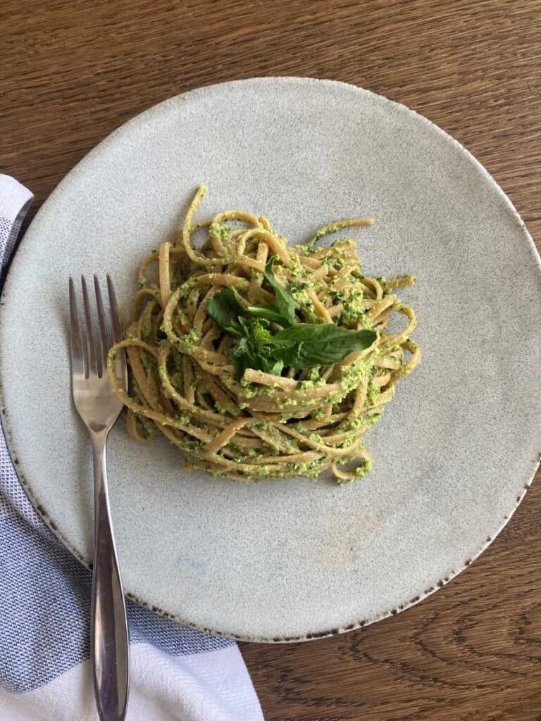 Edamame pasta sauce on whole wheat spaghetti noodles presented on a white plate, topped with basil and a fork on a wood table.