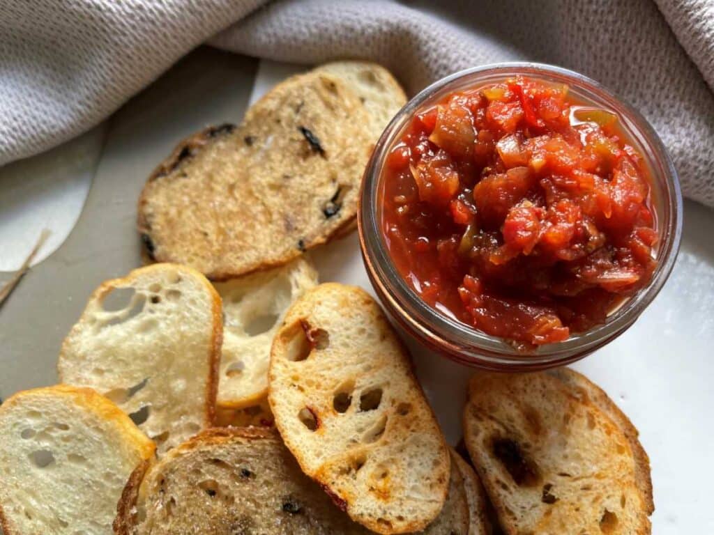 Low sodium salsa surrounded by homemade crackers and a grey tea towel on a white counter.