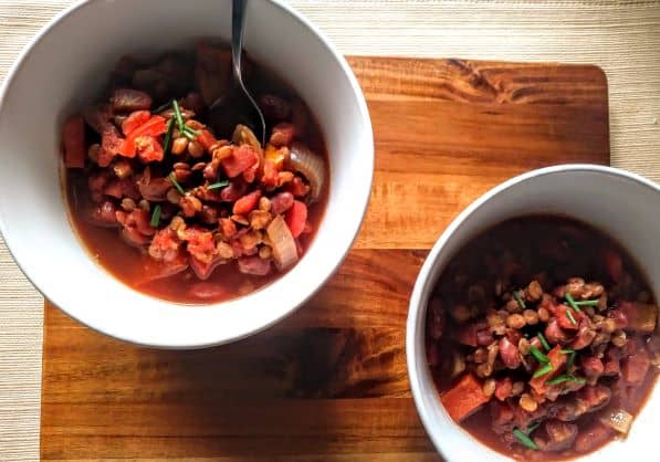 Low sodium instant pot lentil chili displayed in two white bowls on a wood cutting board.  One bowl has a spoon ready to eat.