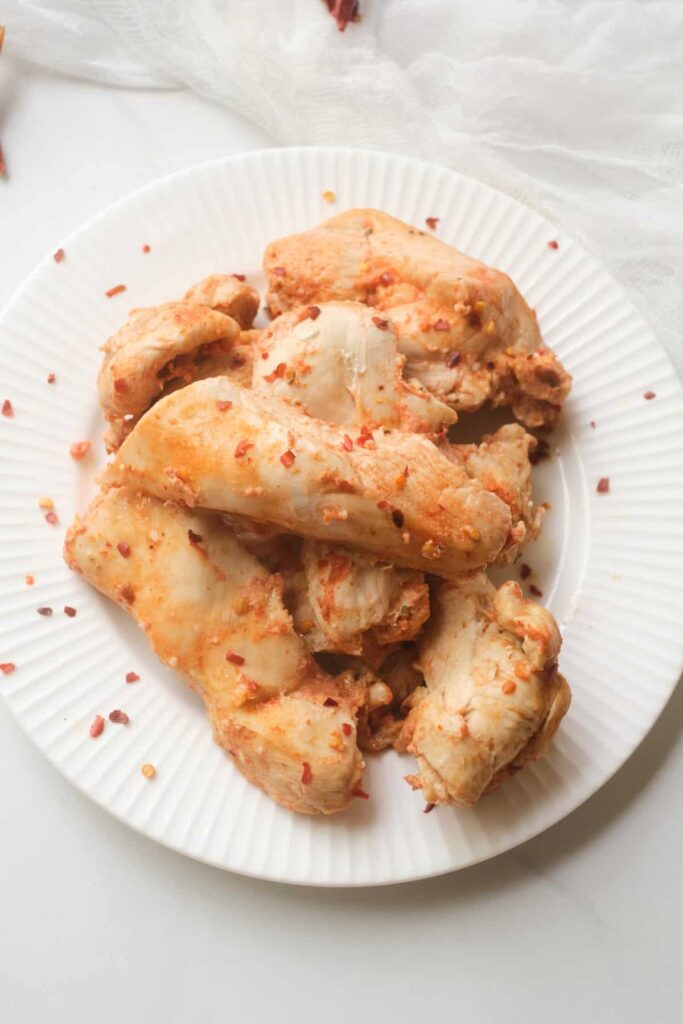 Low sodium instant pot chicken tenders topped with red chili flakes on a white plate displayed on a white table.
