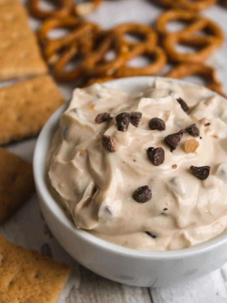 Low sodium cookie dough dip in a white bowl topped with chocolate chips  surrounded by pretzels and graham crackers. 