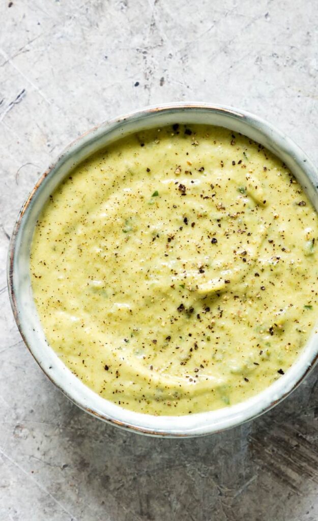 Zucchini low sodium dip topped with red pepper in a white bowl on a white marbled counter.