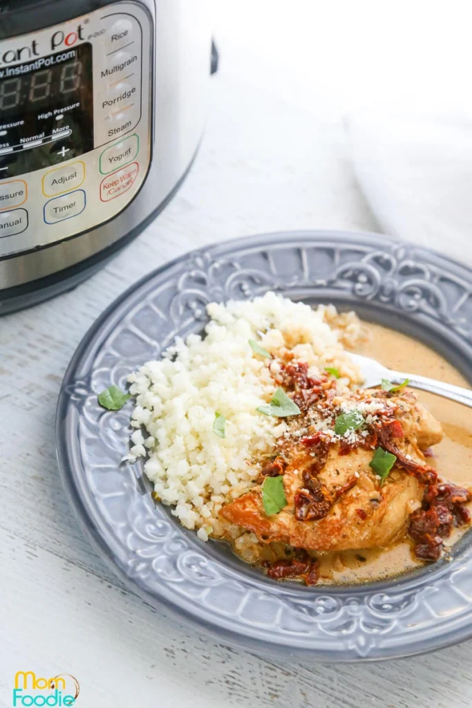 Low sodium instant pot chicken on a blue plate with white rice, and green basil.  Displayed on a white table beside an instant pot. 