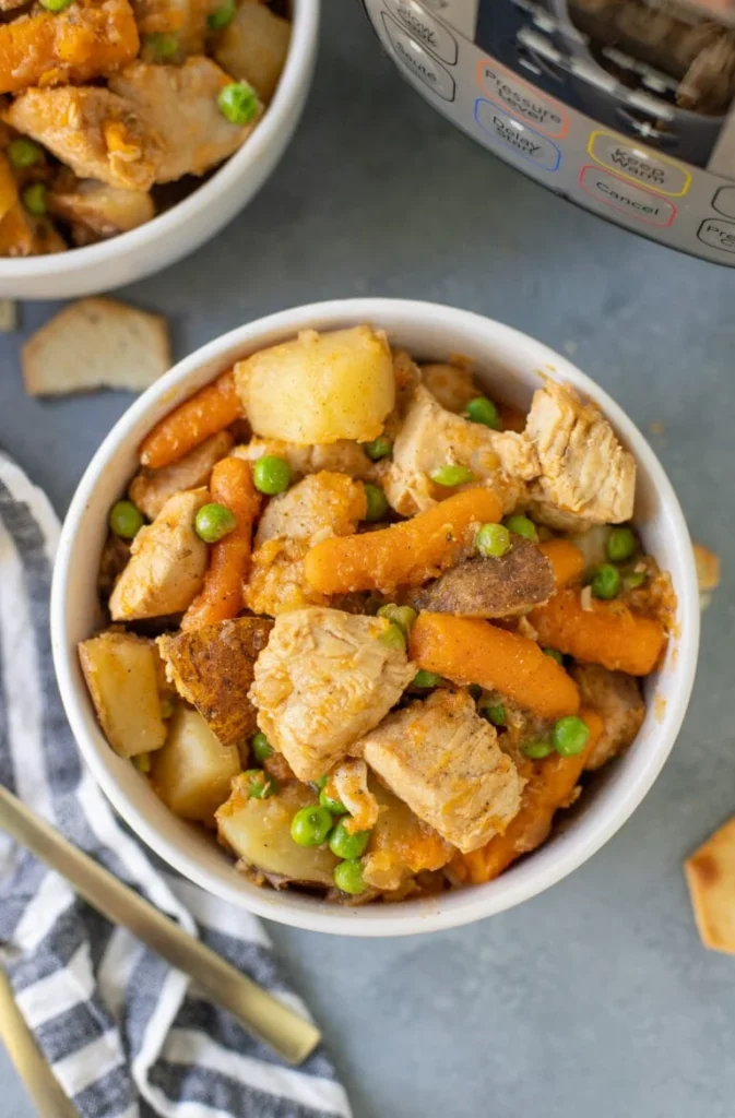 Chunks of chicken, cooked baby carrots, cubed potatoes and green peas in a white bowl.