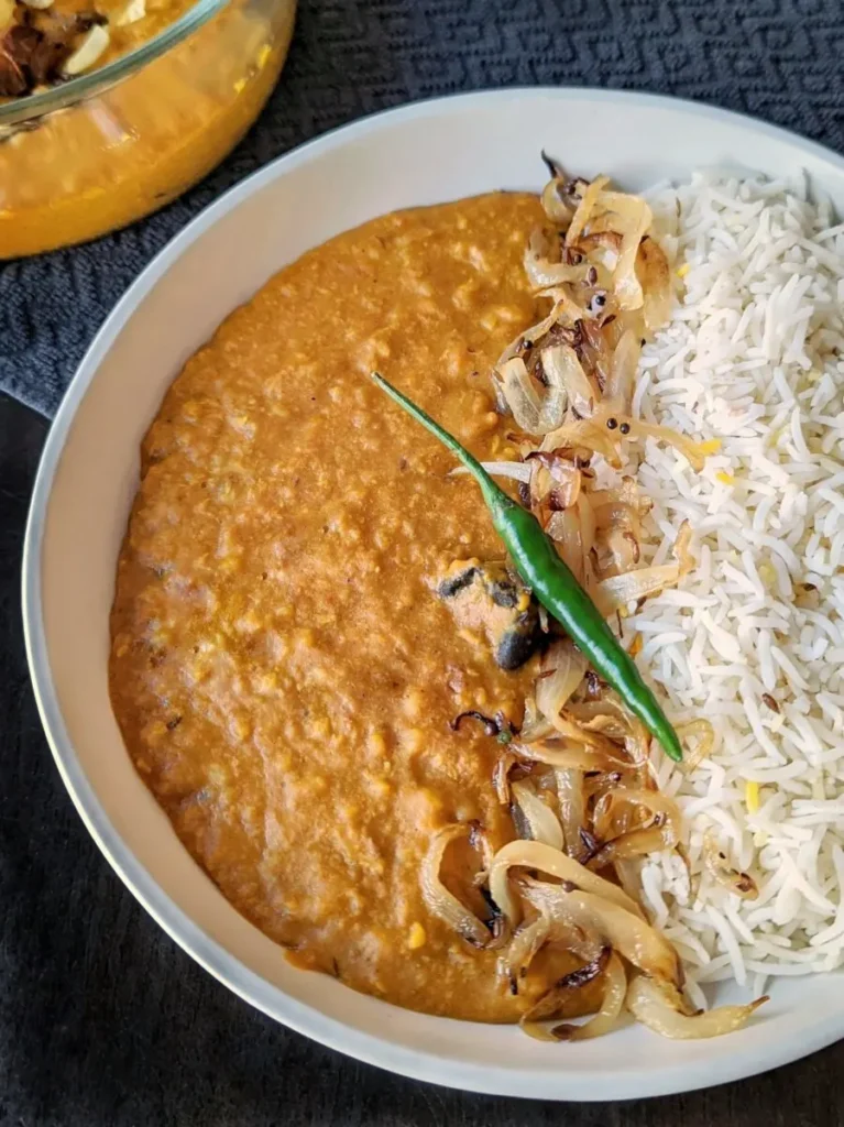 Low sodium instant pot orange dal in a white bowl with half of bowl of white rice and a green chili pepper on top. 