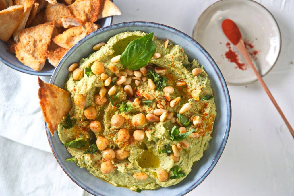 Light green hummus in a blue bowl topped with whole chickpeas and basil.