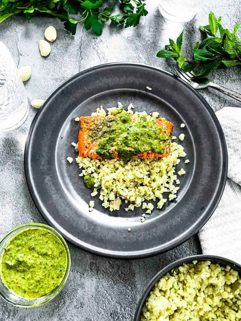 Heart healthy salmon topped with green sauce over cauliflower rice on a blue plate.