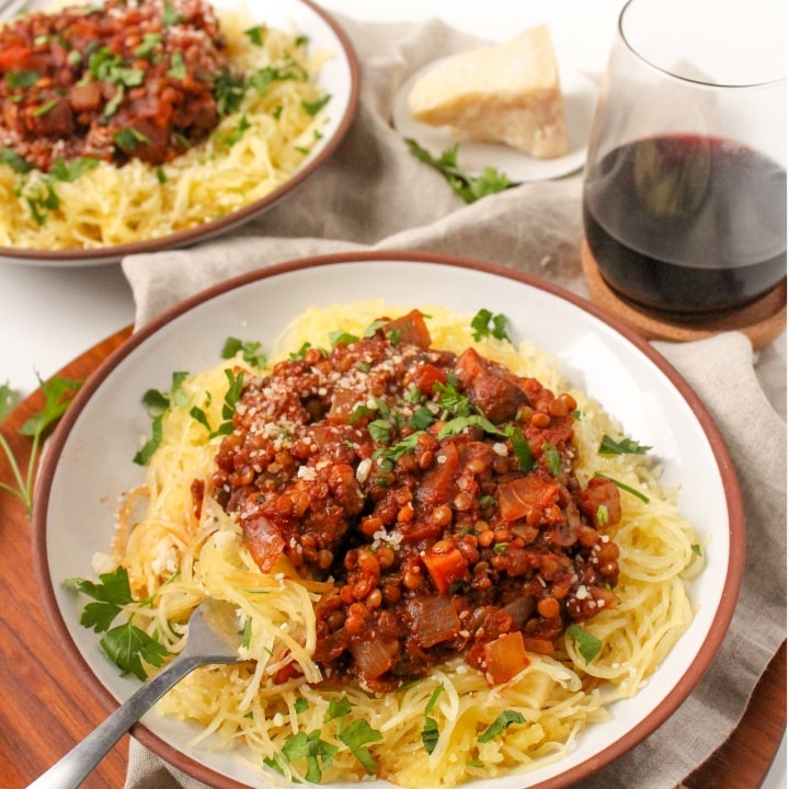 Spaghetti squash noodles in a white bowl with a red rim topped with marina sauce, beside a glass of red wine.