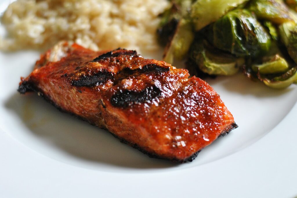 BBQ salmon beside rice and green vegetables on a white plate.