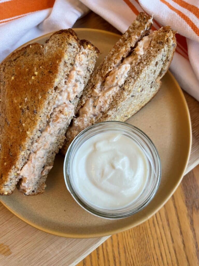 Salmon salad sandwich with low sodium mayonnaise displayed in a mason jar beside the sandwich on a brown plate.