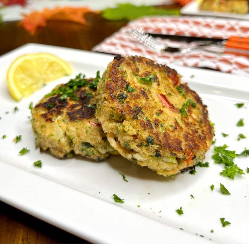 2 salmon fish cakes without potatoes displayed on a white plate with a slice of lime and minced herbs.