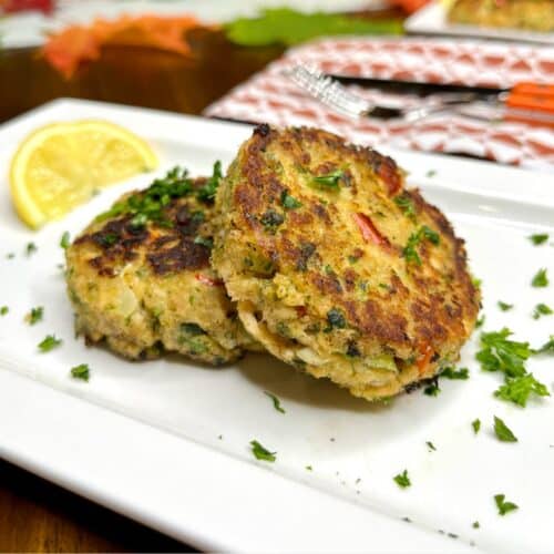 2 salmon fish cakes without potatoes displayed on a white plate with a slice of lime and minced herbs.