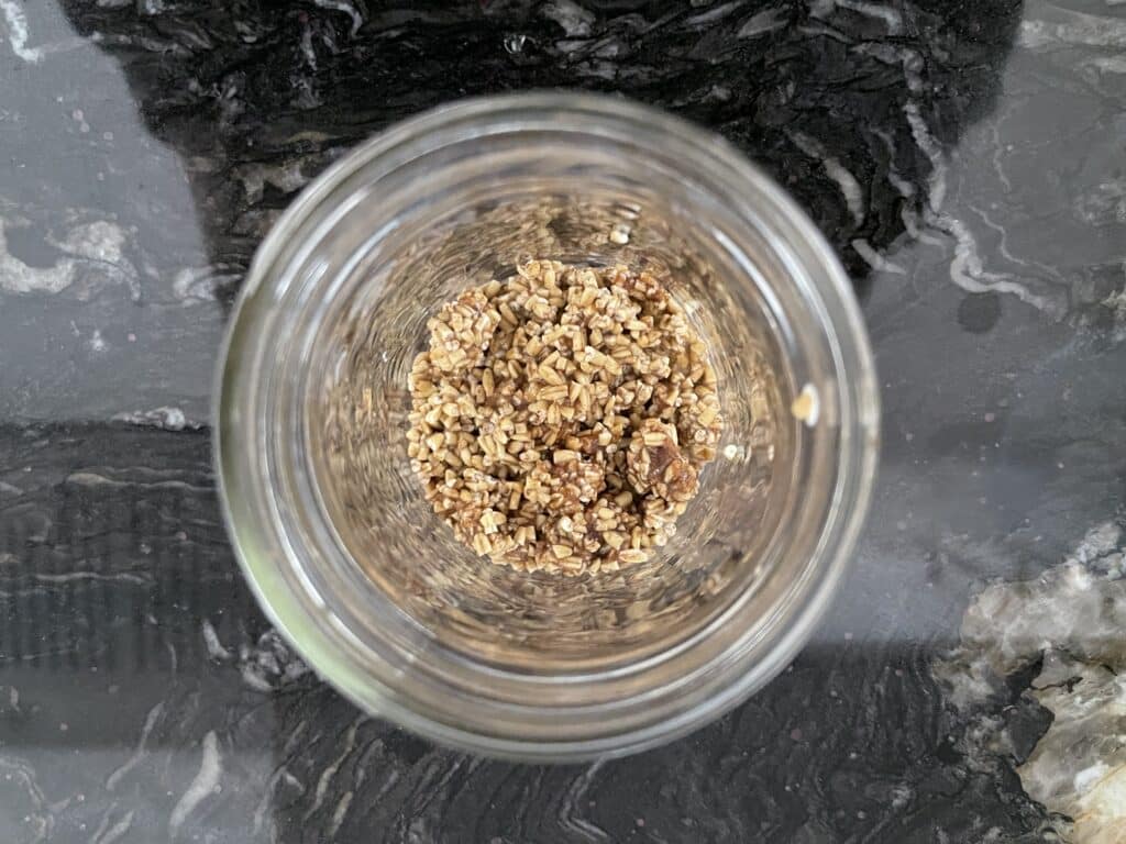 The crust for the cheesecake oatmeal displayed in a mason jar on a black counter.