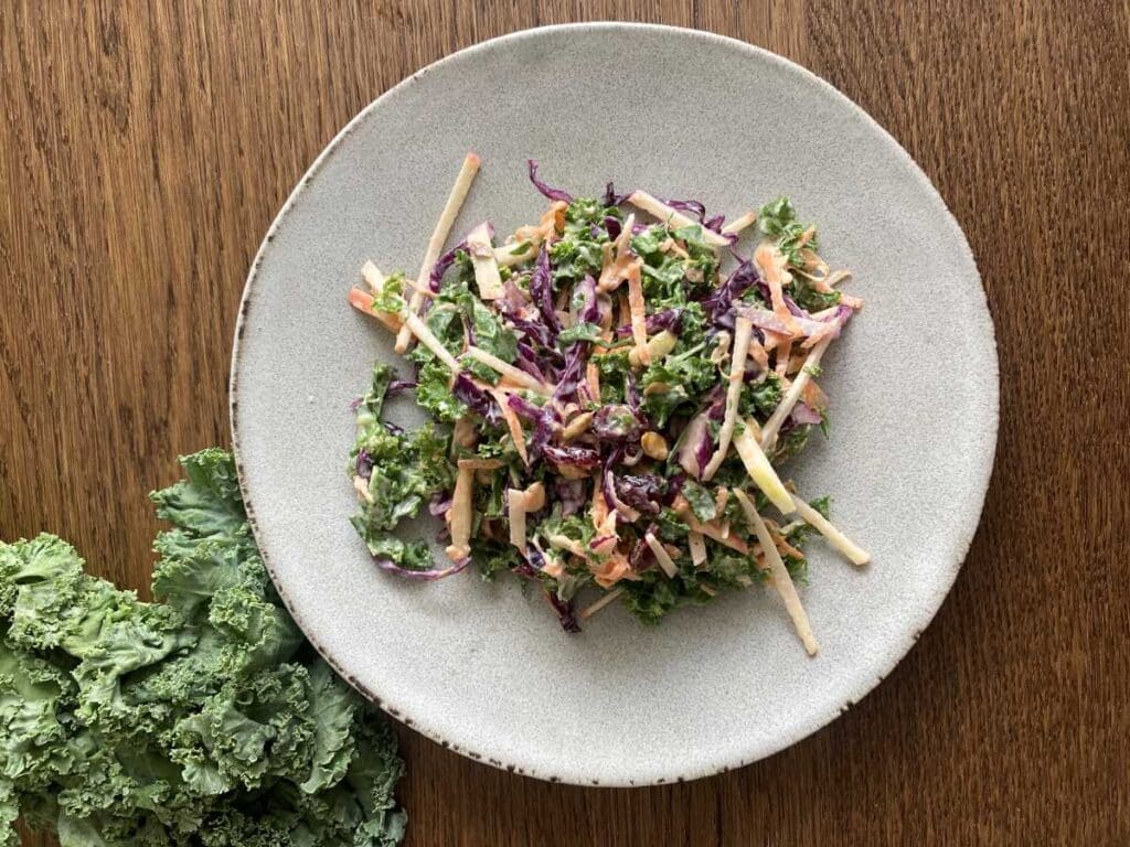 Kale apple slaw presented on a white plate beside a bunch of kale.