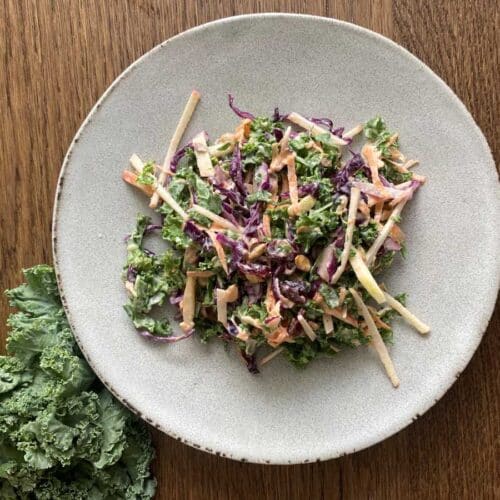 Kale apple slaw presented on a white plate beside a bunch of kale.