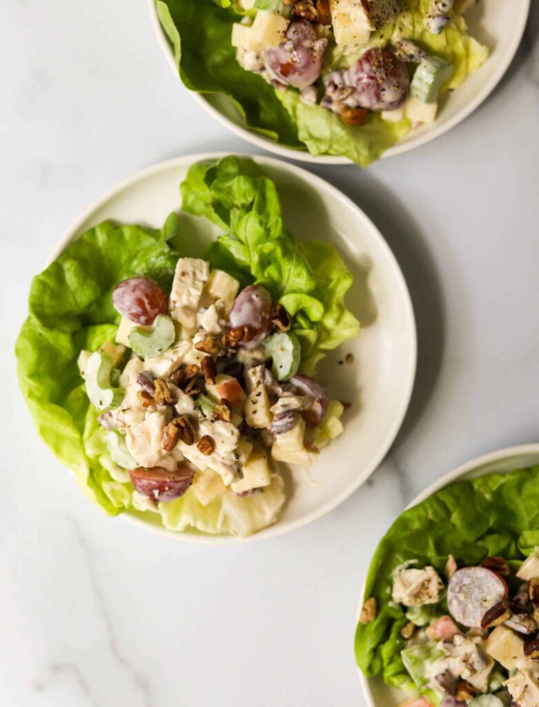 Three white plates of Boston lettuce topped with cubed chicken and grapes in a white sauce.