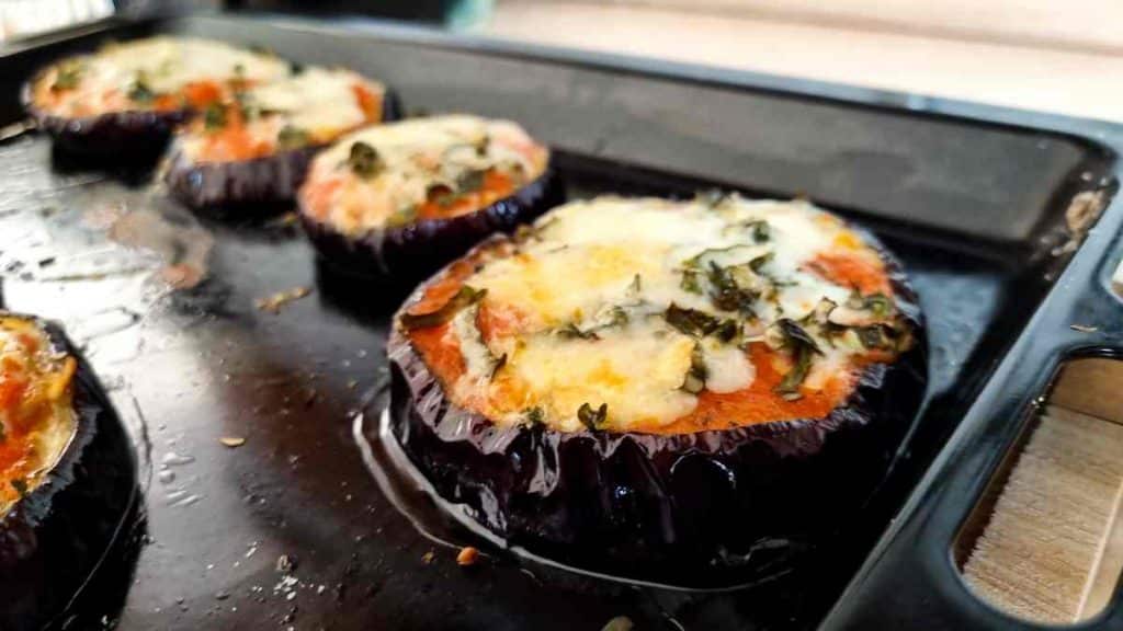 Low sodium dinner eggplant sliced in rounds topped with cheese and tomato sauce presented on a baking sheet.