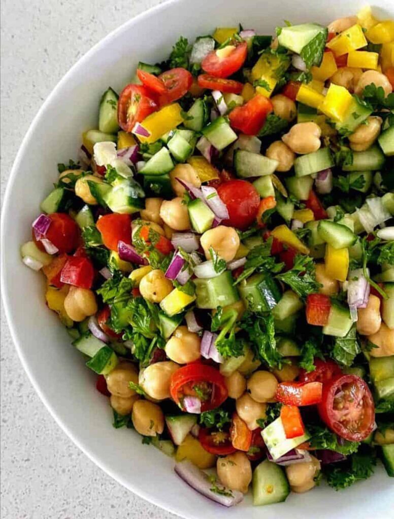 A bowl of low sodium lunch bean salad with chopped cucumber, peppers, chickpeas and sliced cherry tomatoes presented in a white bowl.