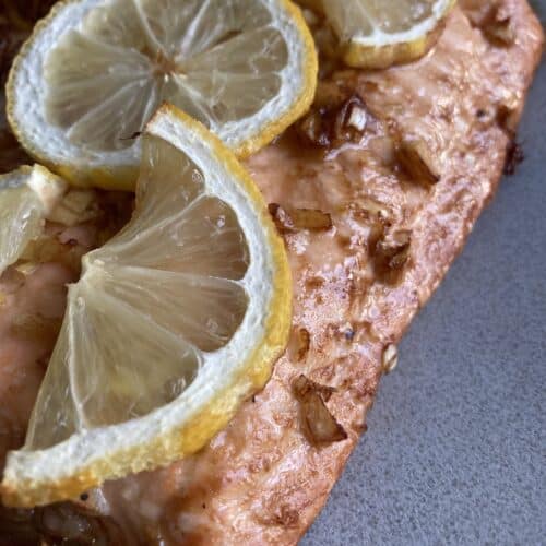 A close up of lemon ginger salmon fillet, topped with lemons.