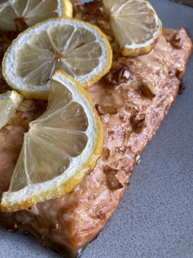 A close up of lemon ginger salmon fillet, topped with lemons.