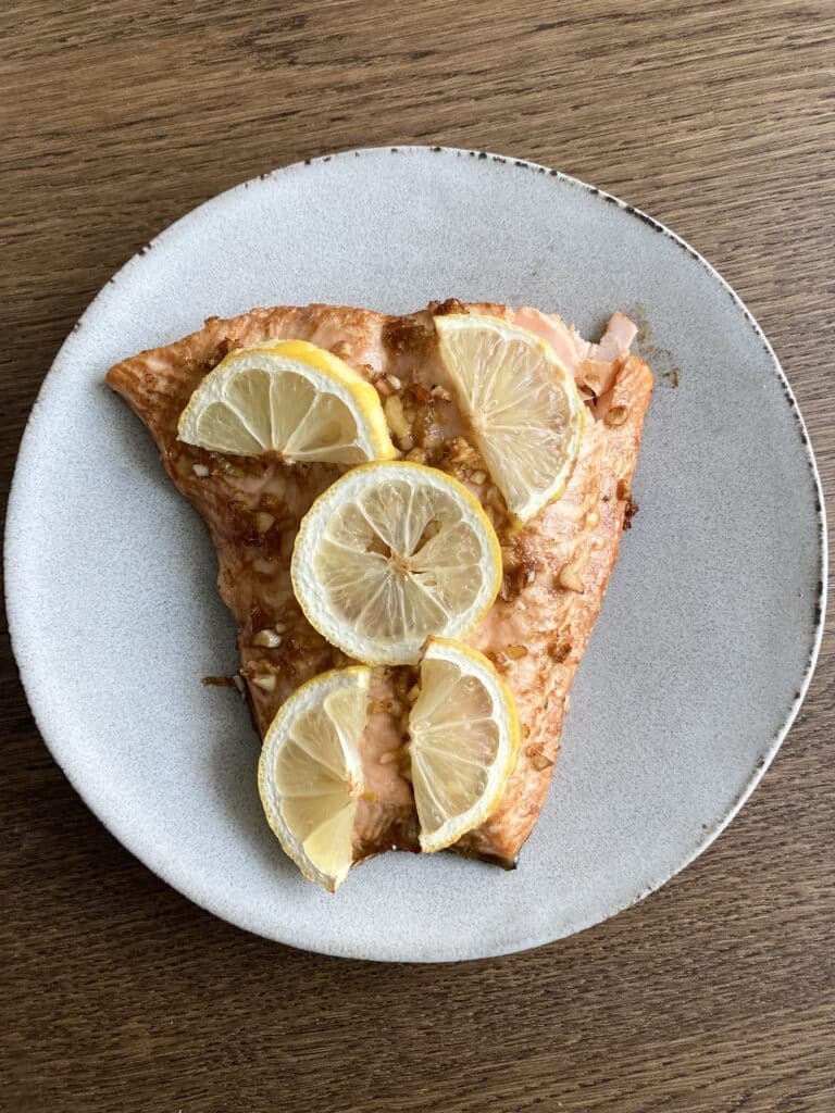 Lemon ginger salmon fillet on a white plate topped with slices of lemon.