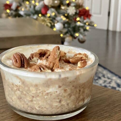 Pecan pie overnight oats in glass container on brown table with a christmas tree in the background.