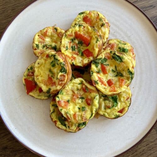 Ricotta egg bites stacked on a white plate on a wood table.