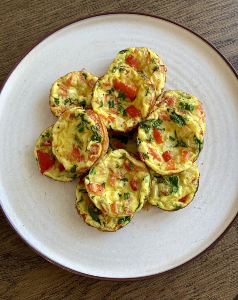 Ricotta egg bites stacked on a white plate on a wood table.