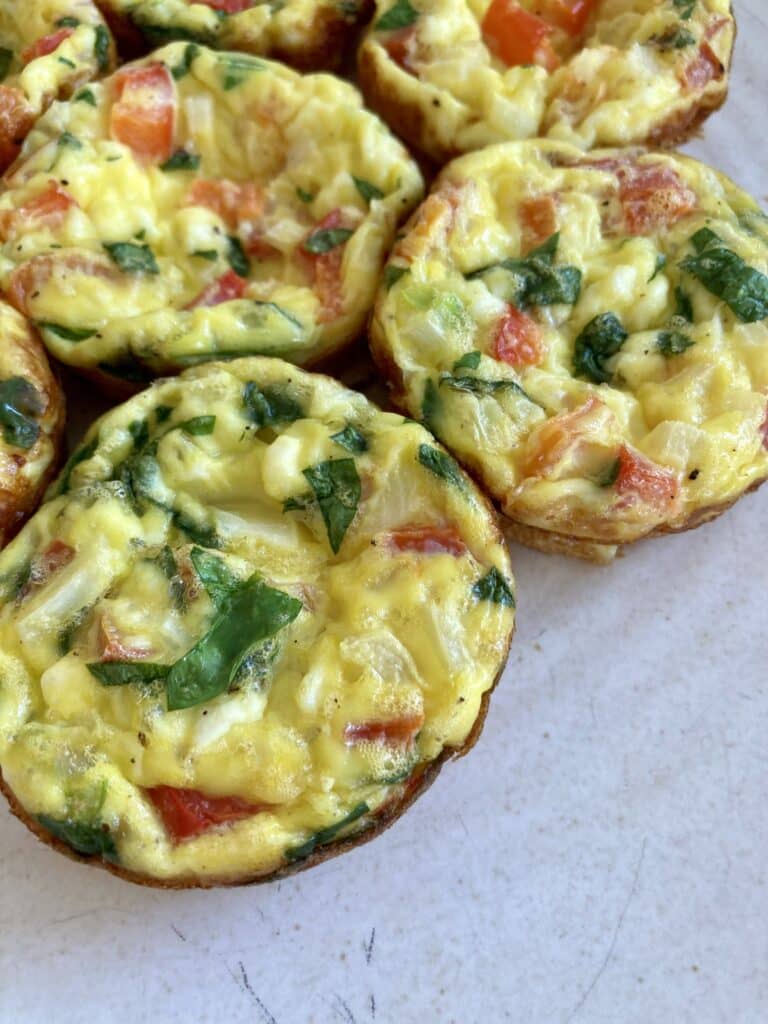 Close up picture of the ricotta egg bites on a white plate full of green spinach and diced red peppers.