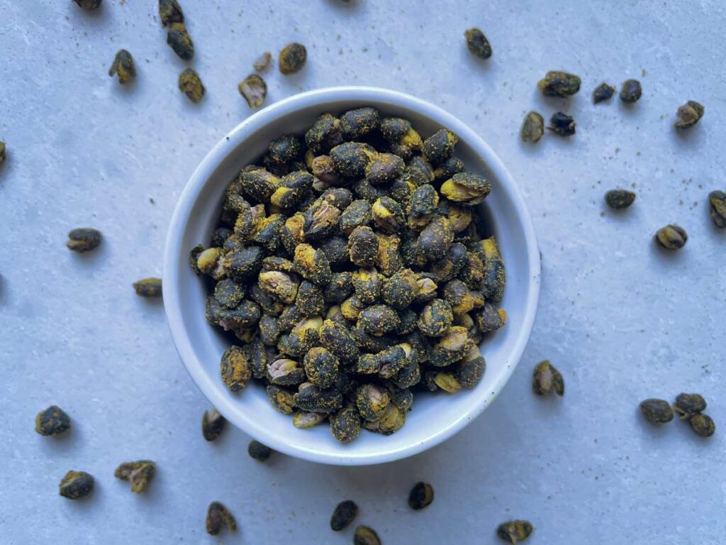 Roasted black beans presented in white bowl on a white counter with roasted beans scattered around it.