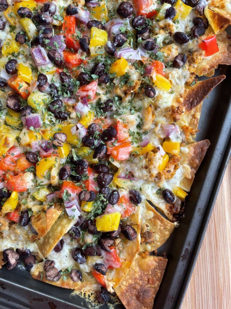 Cooked salmon nachos presented on baking sheet on a wood cutting board.