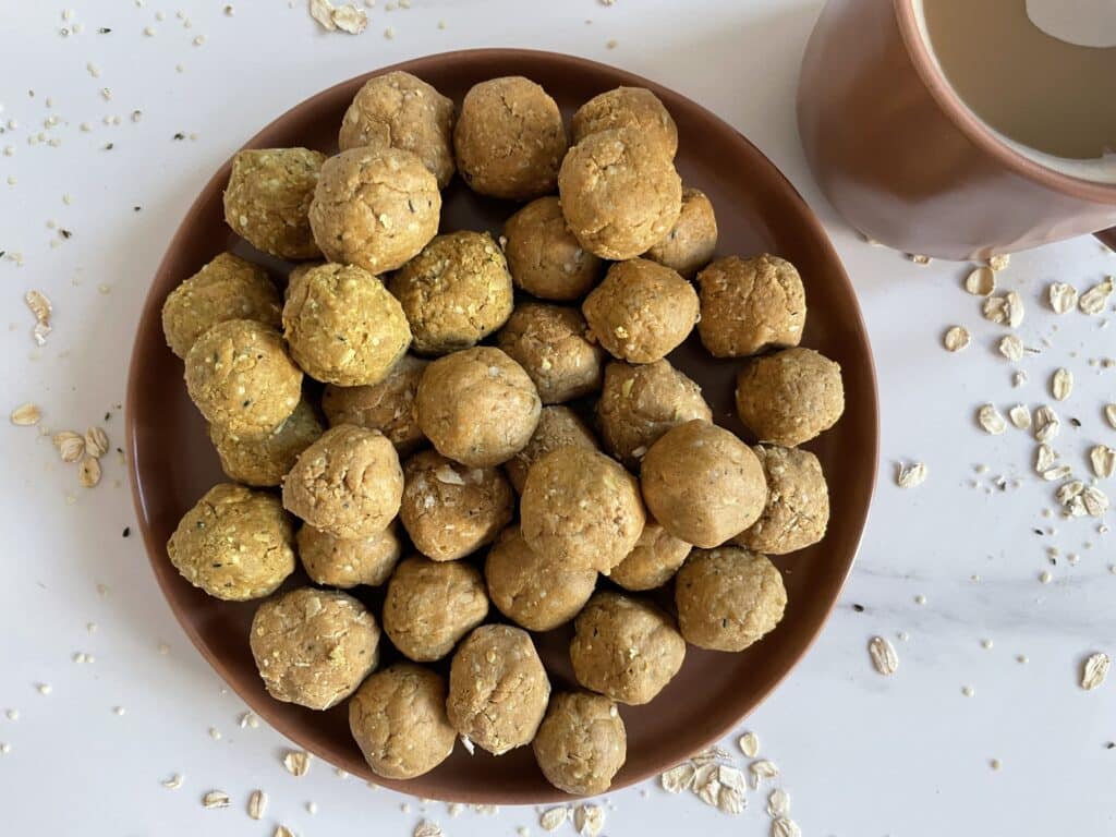 Turmeric energy balls displayed on a brown plate on a white countertop beside a brown mug of coffee.