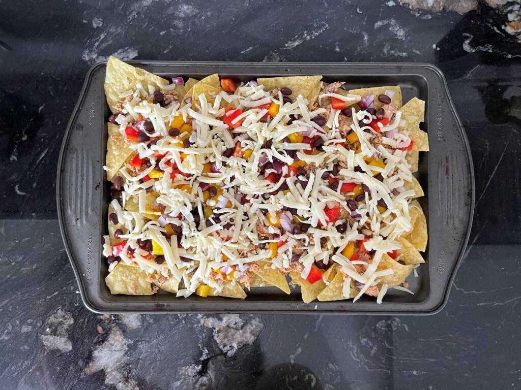 Salmon nachos presented on baking sheet layered with salmon, vegetables, beans and cheese.