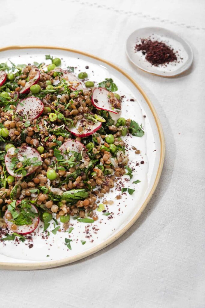 Green lentil salad presented on a white plate with green beans, radishes and asparagus.