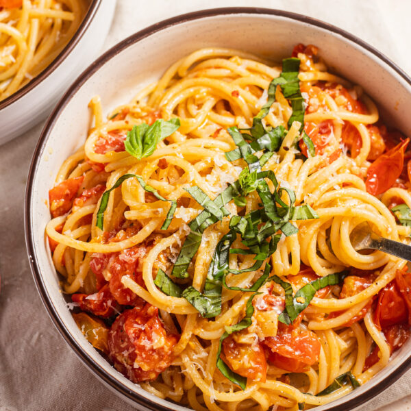 Cooked tomatoes in a low sodium pasta dish in a white bowl topped with fresh herbs.