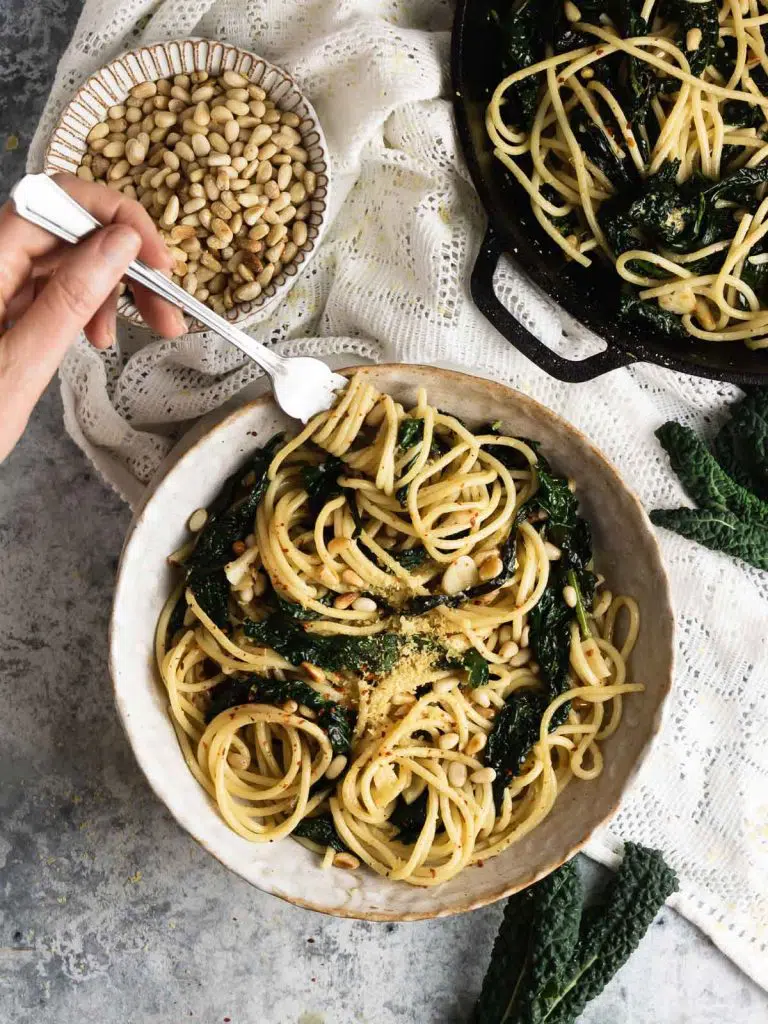 Spaghetti noodles with sautéed kale in a beige bowl spiraled around a fork, ready to eat.