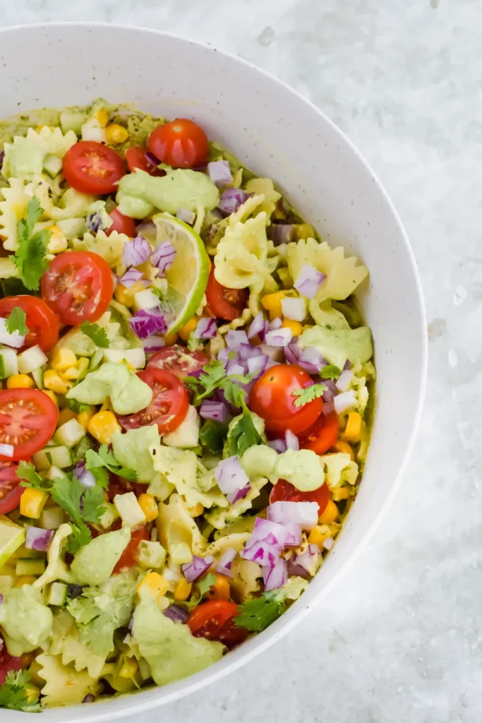 Low sodium pasta dish with cilantro dressing gives these bowtie pasta noodles a ting of green, topped with sliced cherry tomato, lime and fresh herbs.