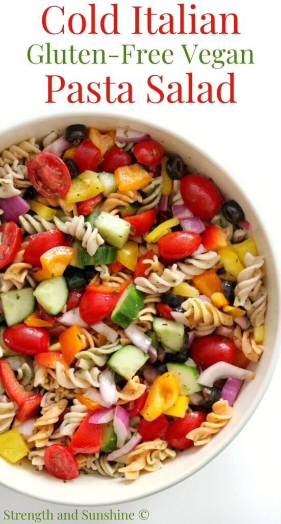 Cold low sodium pasta salad presented in a big white bowl with tomatoes, chopped cucumbers, peppers, olives and rotini noodles.