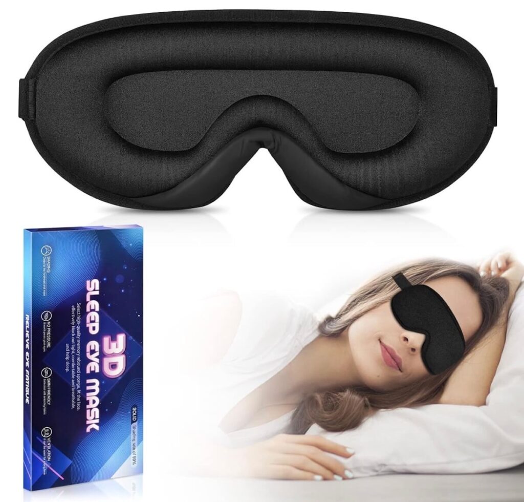 A black contour sleeping mask shown in a box, open, and on a person sleeping. 