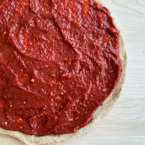 Low sodium pizza sauce on a whole wheat pizza crust on a wood cutting board.