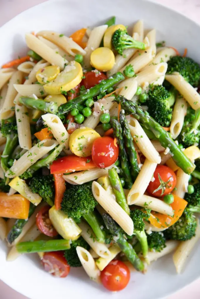Fresh low sodium pasta salad using penne noodles, cherry tomatoes, asparagus and green peas presented in a white bowl.