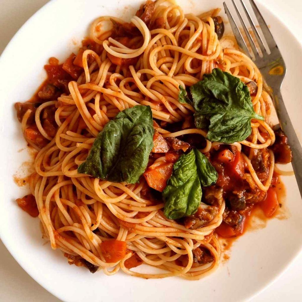 Low sodium pasta dish in tomato sauce topped with fresh basil on a white plate beside a fork.